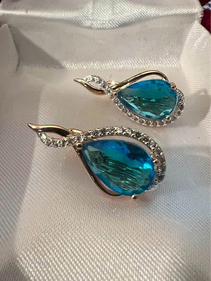 A pair of 14k rolled gold earrings with a teardrop blue topaz surrounded by a halo of pave crystals.