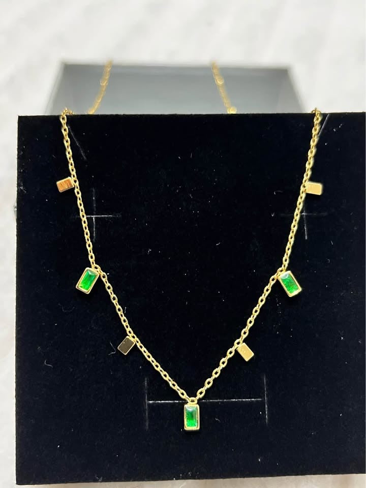 Straight-on view of an 18K gold vermeil emerald necklace, showcasing green rectangular gems in a black box.