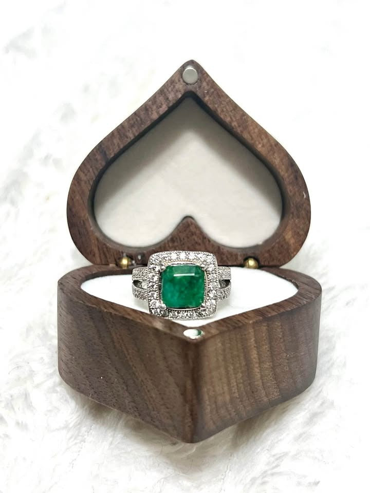 A stunning 2 CT natural emerald ring with a diamond halo, displayed in an open heart-shaped wooden box.