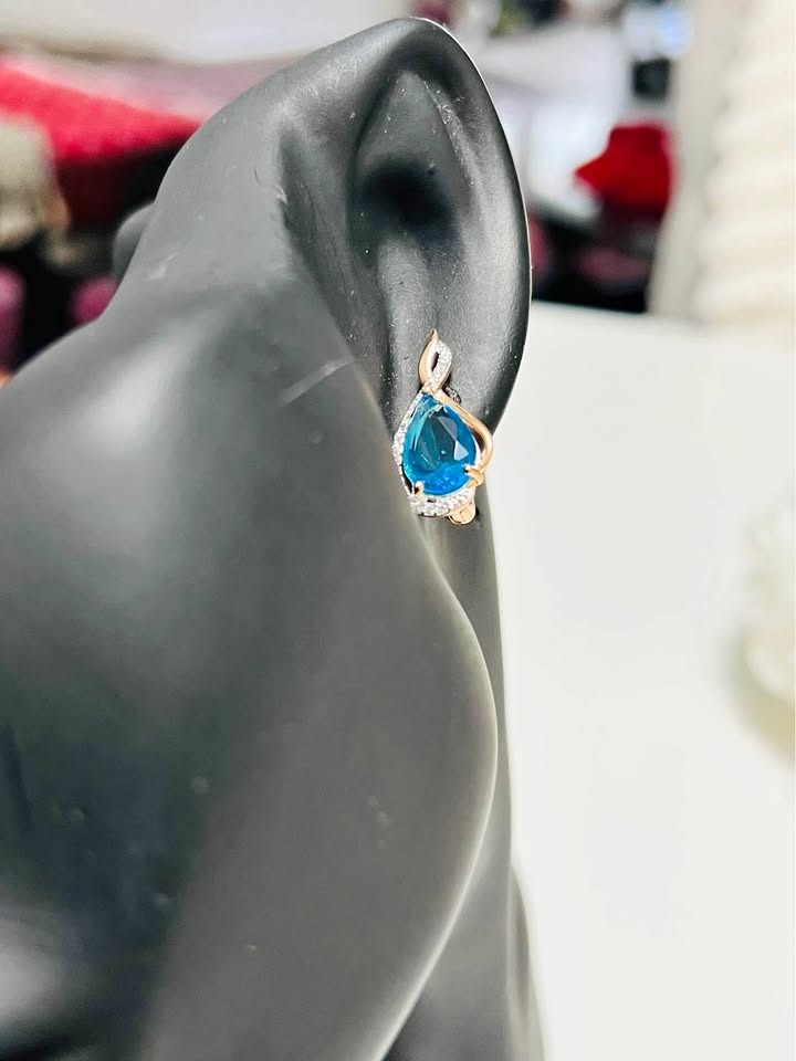 A model wearing a 14k rolled gold earring with a stunning teardrop blue topaz and pave crystals.