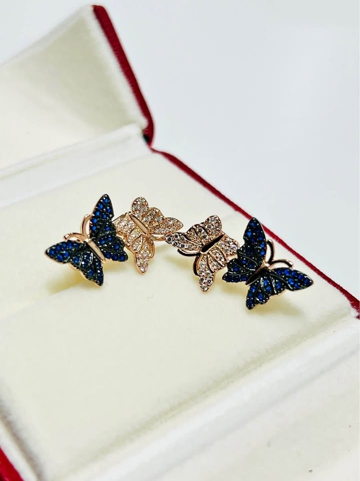 Detailed view of 14k rolled gold butterfly stud earrings, featuring sparkling pave-set blue and clear crystals.