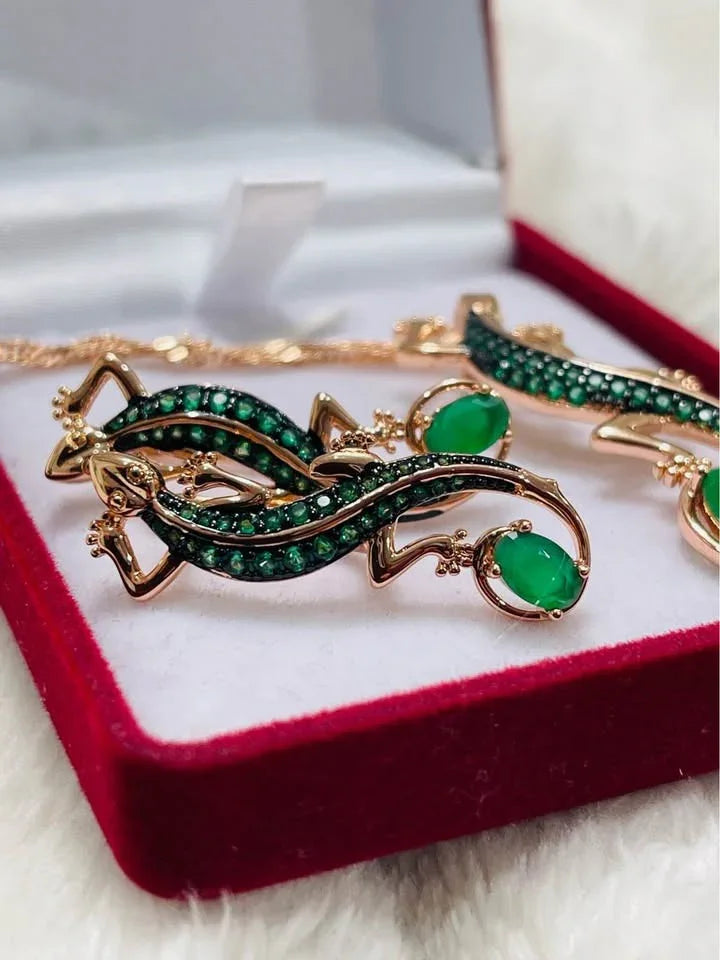Close-up of rolled gold 585RG salamander earrings, richly adorned with green emeralds, in a jewelry box.