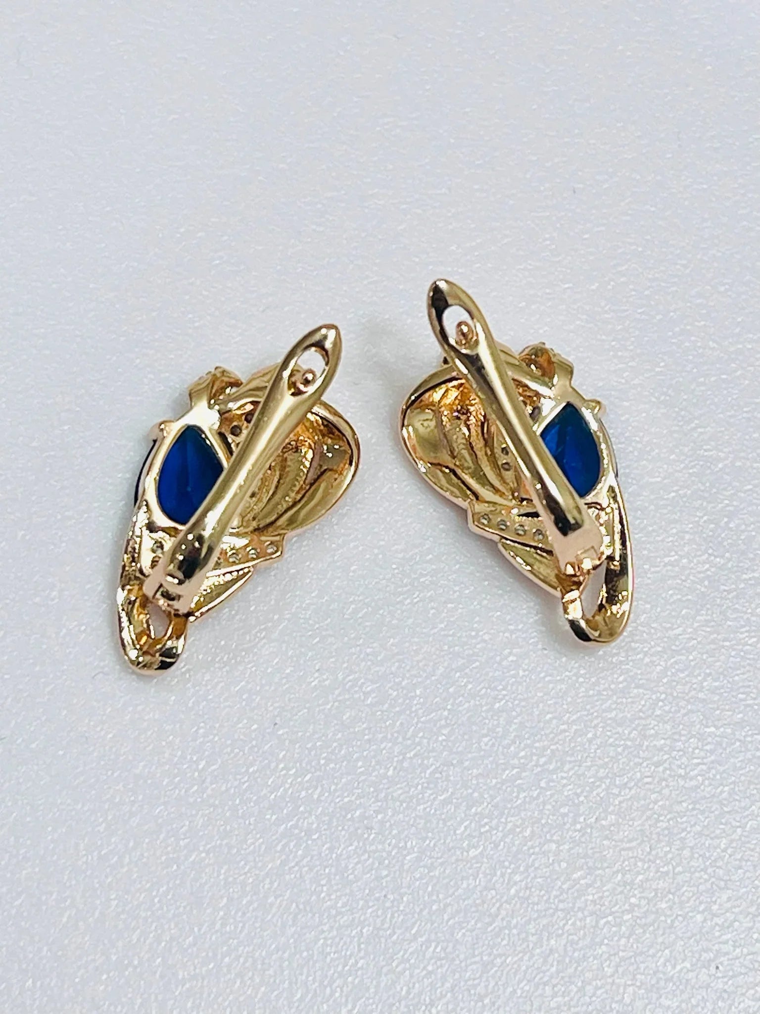 Gold earrings with blue stones on a light gray background