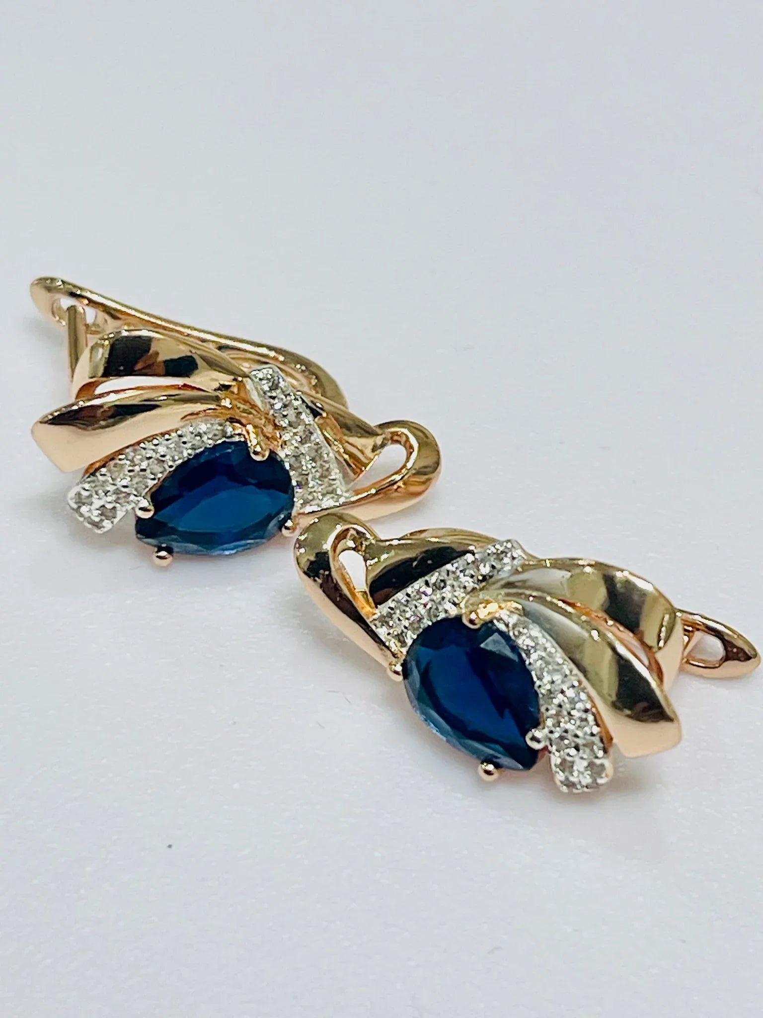 Gold earrings with blue gemstones on a light gray background