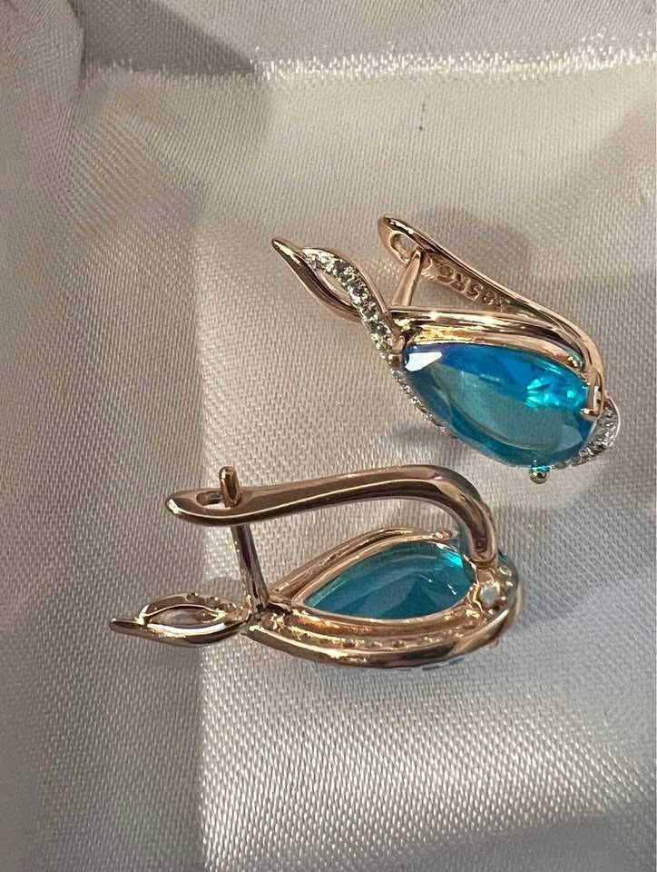 Elegant 14k rolled rose gold dangle earrings with a teardrop-shaped blue topaz and a crystal accent.