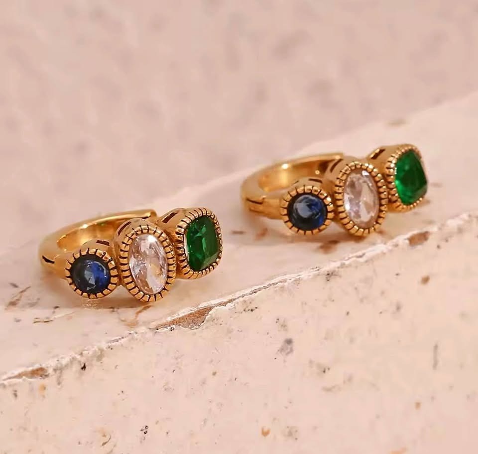 Pair of multi-gemstone huggie hoop earrings with bezel-set emerald, clear topaz, and sapphire stones.