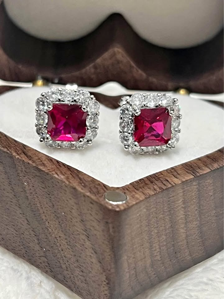 Close-up of dazzling sterling silver ruby stud earrings, square cut with diamond halo, in wooden box.