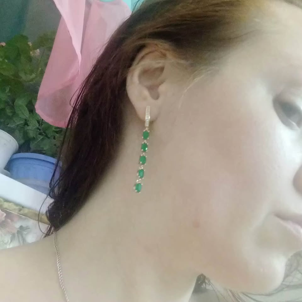 A woman wearing 14K 585RG stamped long dangle earrings featuring a beautiful chain of green emerald gemstones.