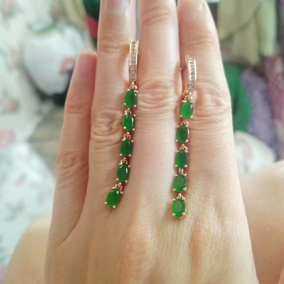 14K 585RG stamped long dangle earrings with multiple oval-cut emeralds and a diamond accent, held on a hand.
