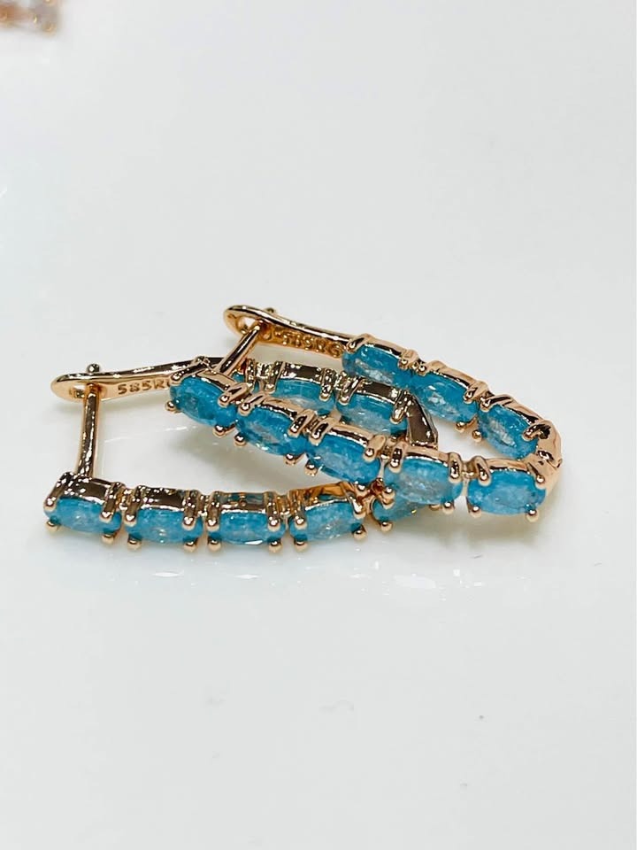 A pair of 14k rose gold-filled V-shaped hoop earrings with a beautiful cascade of blue tourmaline gemstones.