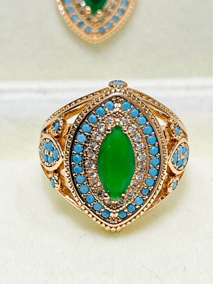 A close-up of a 14K RG585 stamped ring with a marquise-cut emerald center, surrounded by turquoise and CZ stones.