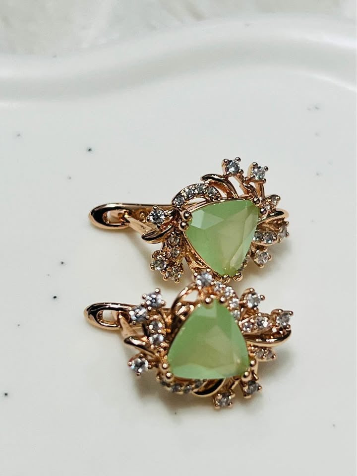 Angled view of artisan 14k rolled gold earrings with natural green prehnite and CZ gemstones on a white background.