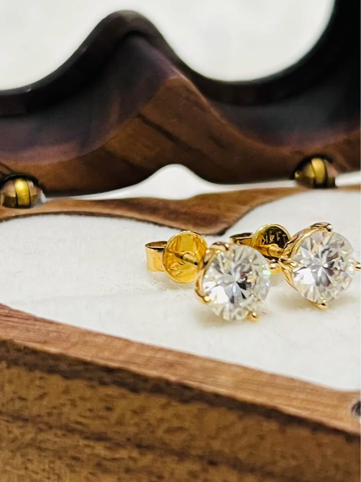 Close-up of dazzling 14k gold Moissanite stud earrings in a elegant wooden jewelry box, showcasing their brilliance.