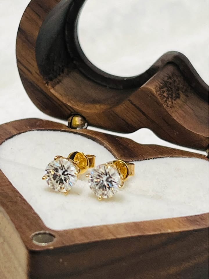  Top view of two brilliant 14k yellow gold Moissanite stud earrings resting in a beautiful wooden jewelry box.