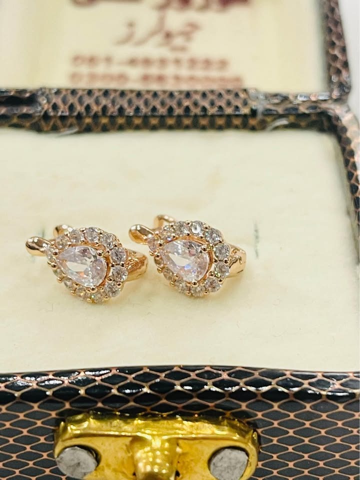 Close-up of 14k rose gold small earrings with a radiant white center stone and cluster halo, in a box.