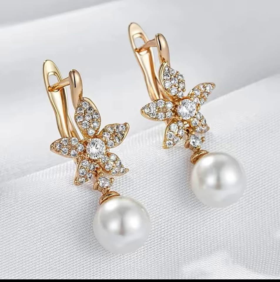 Front view of beautiful 14K gold dangle earrings, featuring flower designs with sparkling stones and white pearls.