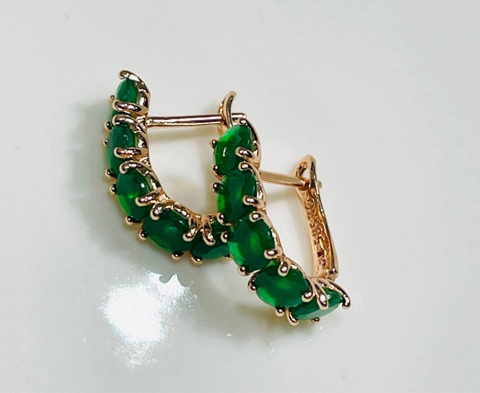 Angled view of 14k rolled gold huggy hoops, featuring a continuous line of beautiful emeralds.