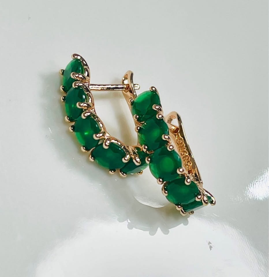 Full pair of 14k rolled gold huggy hoops featuring oval emeralds, elegantly displayed on a white surface.