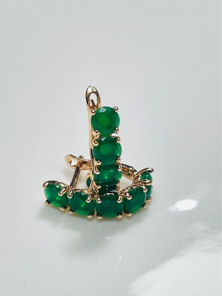  A pair of 14k rolled gold huggy hoops with vibrant emeralds, shown from a side perspective on a white surface.