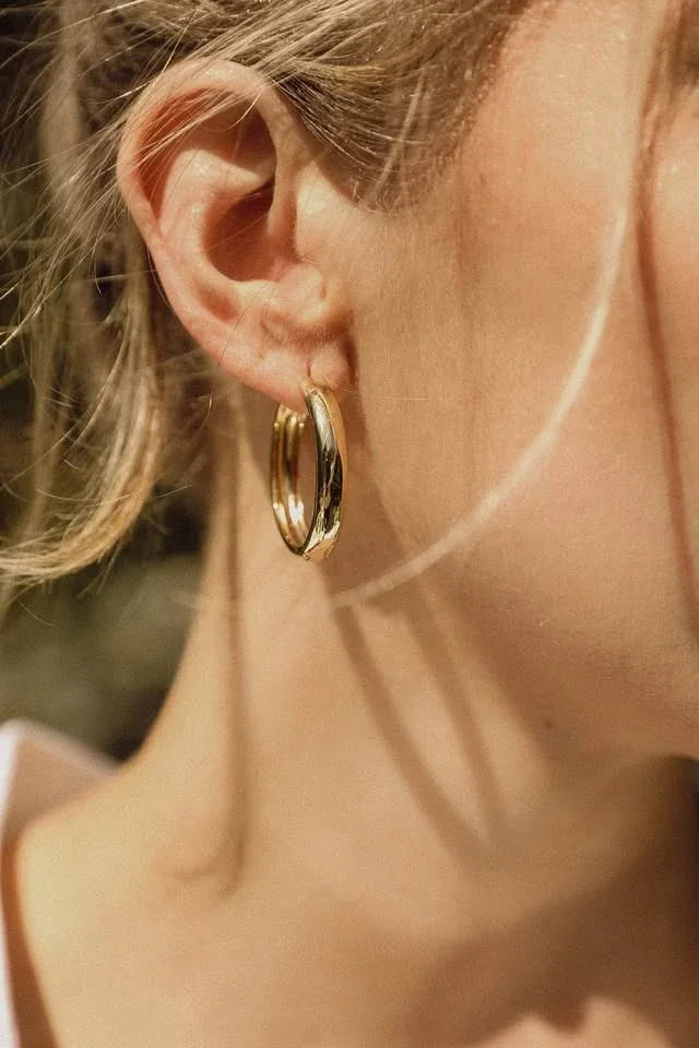 A close-up of a person wearing a simple yet elegant 18K gold vermeil hoop earring.
