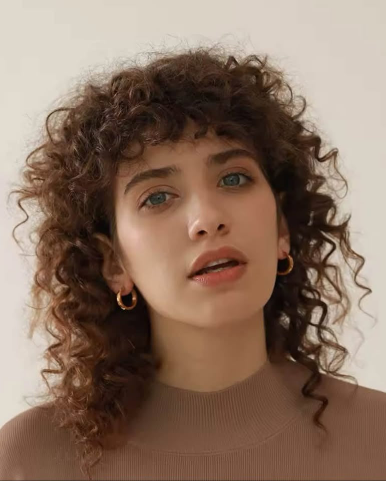 A woman with curly hair wearing elegant 18K gold vermeil waterproof Julia hoops, showcasing their subtle style.