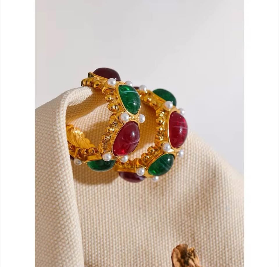 Elegant 18k gold vermeil East West earrings with green and red gems, accented with pearls, resting on natural fabric.