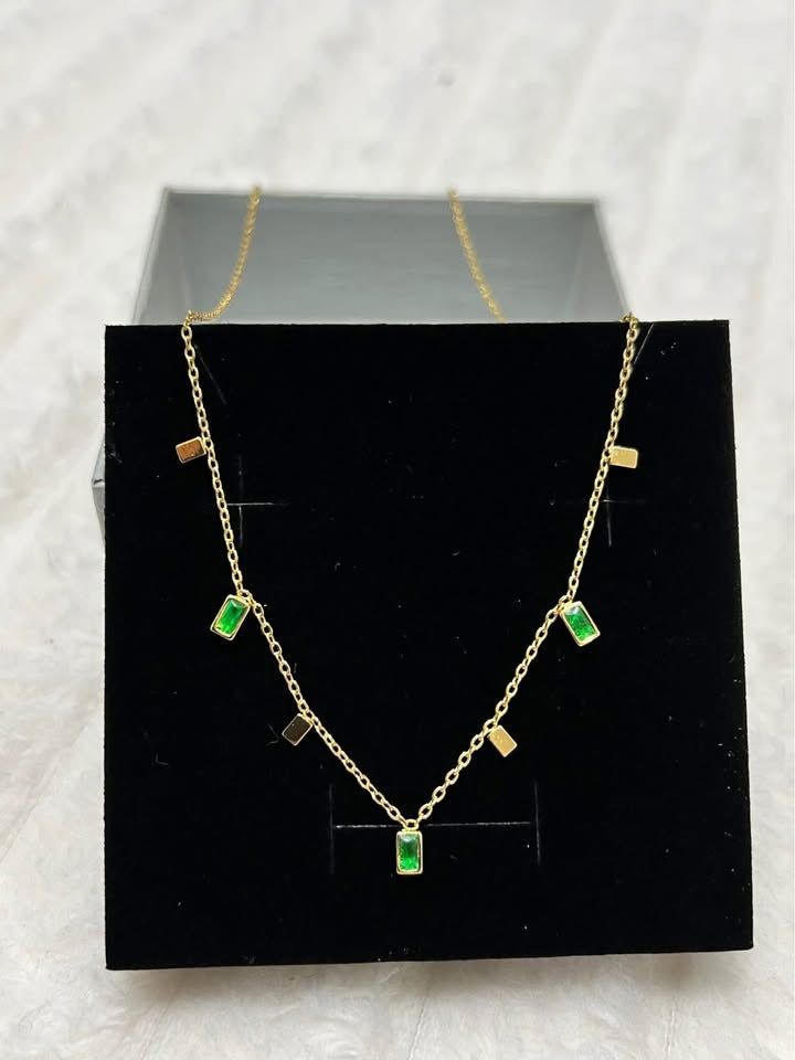 Close-up angled view of an 18K gold vermeil emerald necklace, featuring vibrant green gems in a black jewelry box.