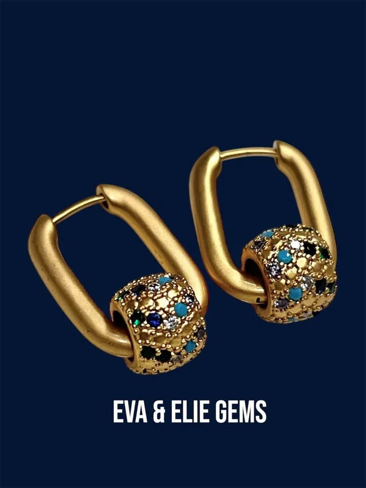 Angled view of a pair of gold vermeil rolling ball earrings with multi-colored rhinestones on a dark blue background.