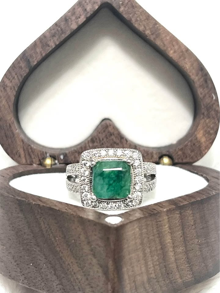 Front view of a 2 carat natural emerald ring with diamond halo and split shank band in a heart-shaped box.