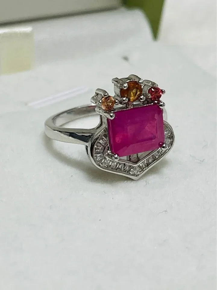Angled view of a 3 carat natural ruby ring with colorful sapphire accents and heart halo in box.