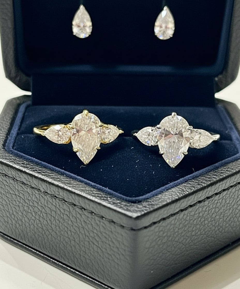 Angled view of two 4 carat pear moissanite rings, gold and silver, sparkling beautifully in a wooden heart box.