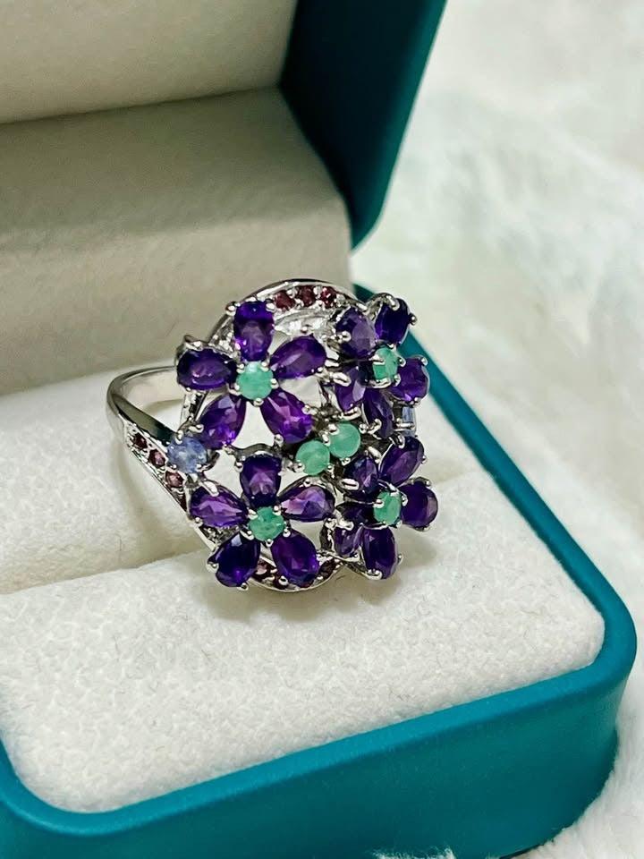  Elegant sterling silver ring featuring natural amethyst and emerald gemstones arranged in a flower design.