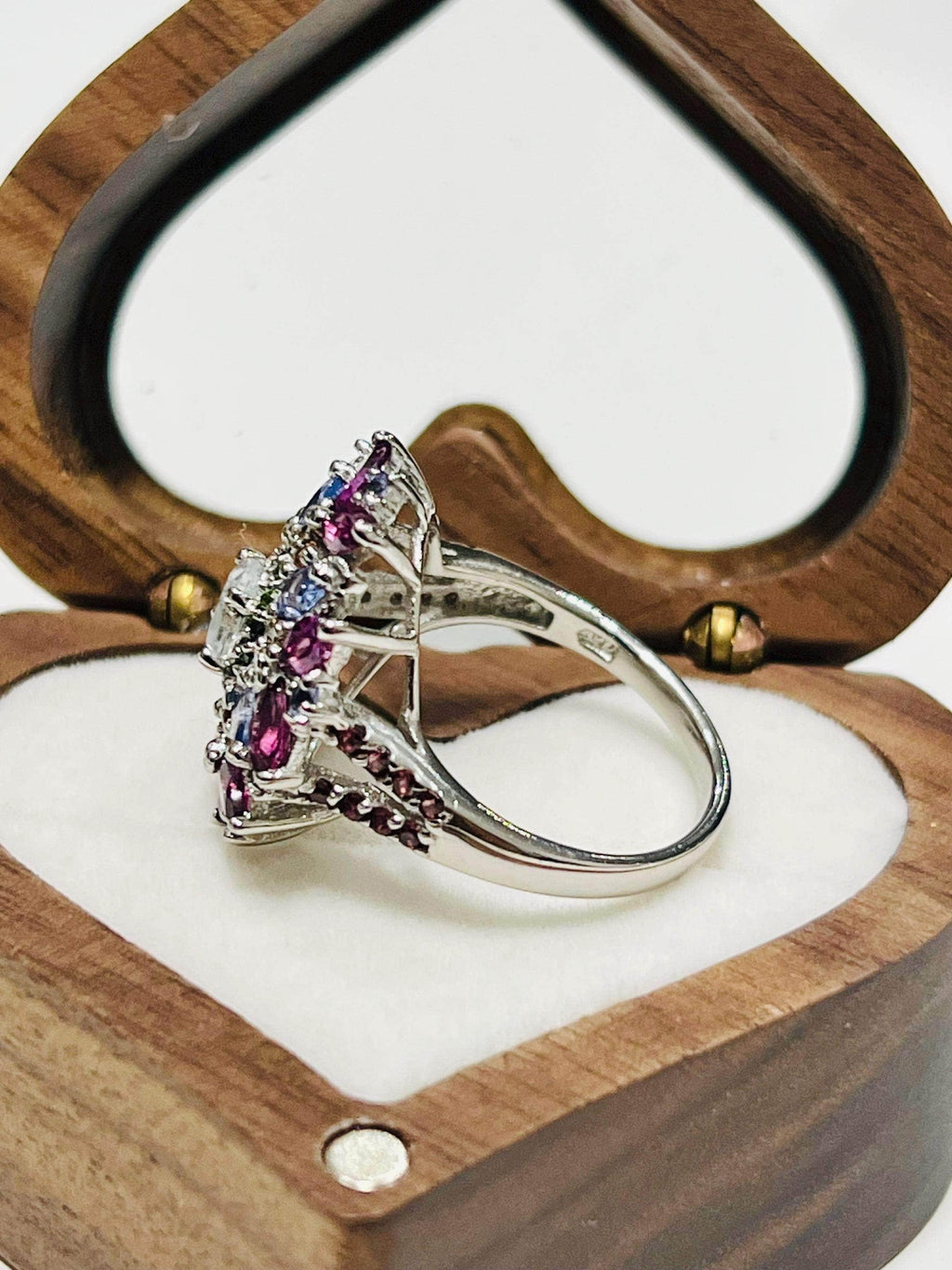 Profile view of a vibrant multi-gemstone floral ring with aquamarine, garnet, and tanzanite in a heart-shaped box