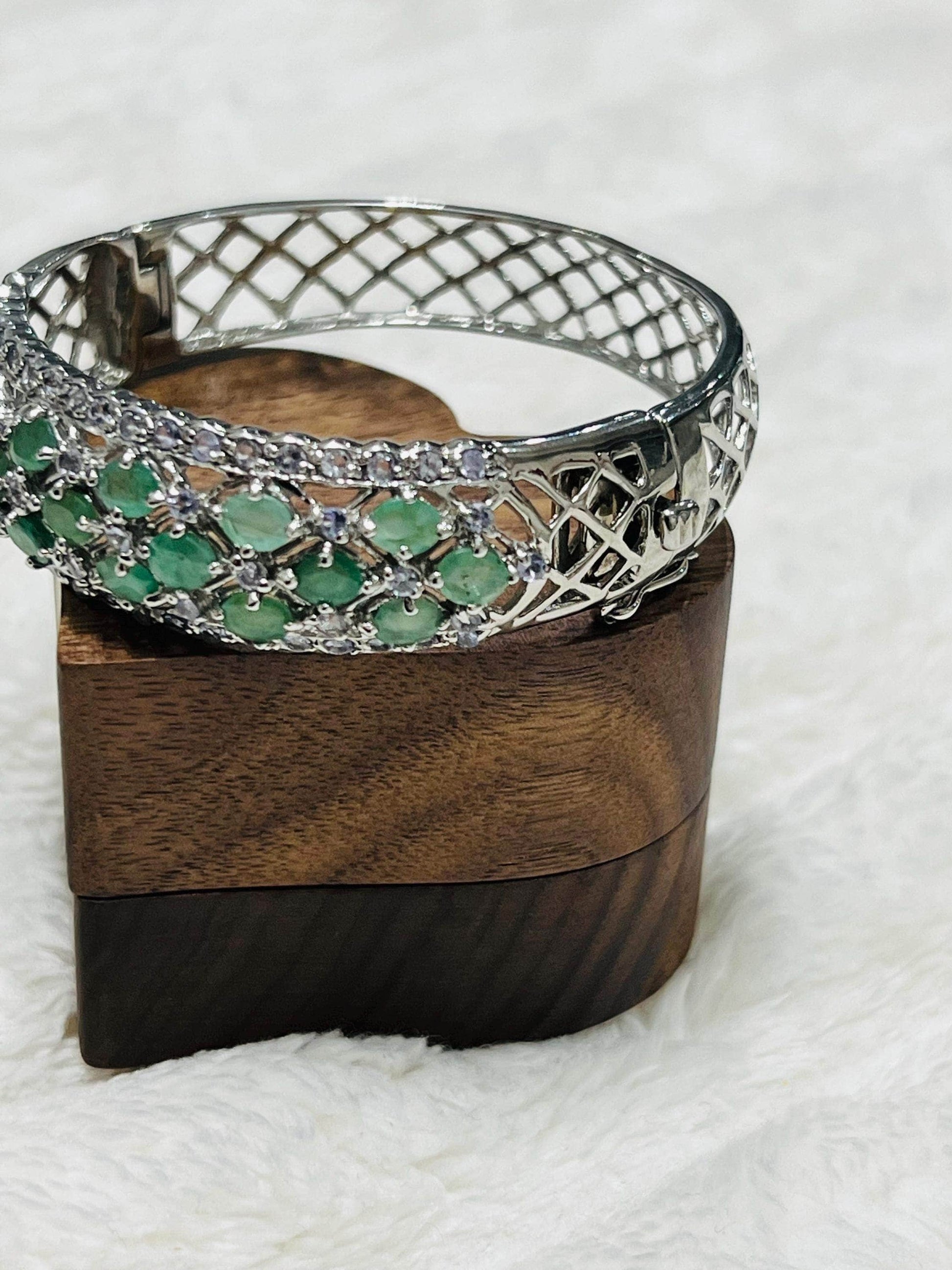 Elegant Aztec emerald and tanzanite bracelet with a captivating design, showcased on a wooden stand.