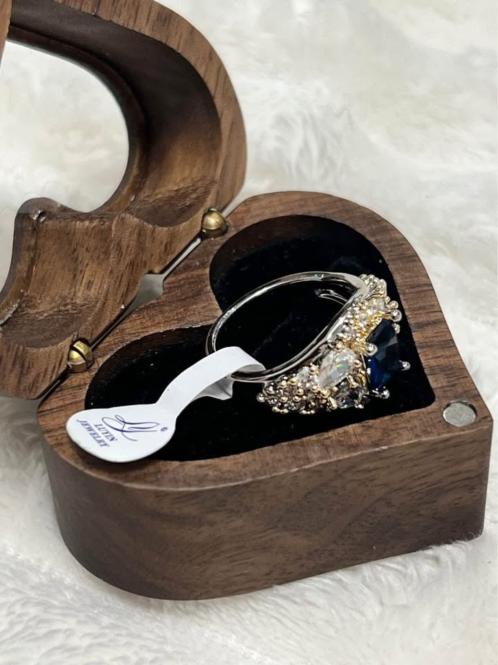  Top-down angled view of a beautiful shining sapphire and diamond ring with tag in a wooden heart box.