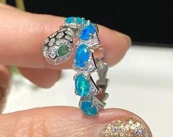 Close-up view of a unique blue opal snake ring held, showcasing intricate detailing and brilliant gems.