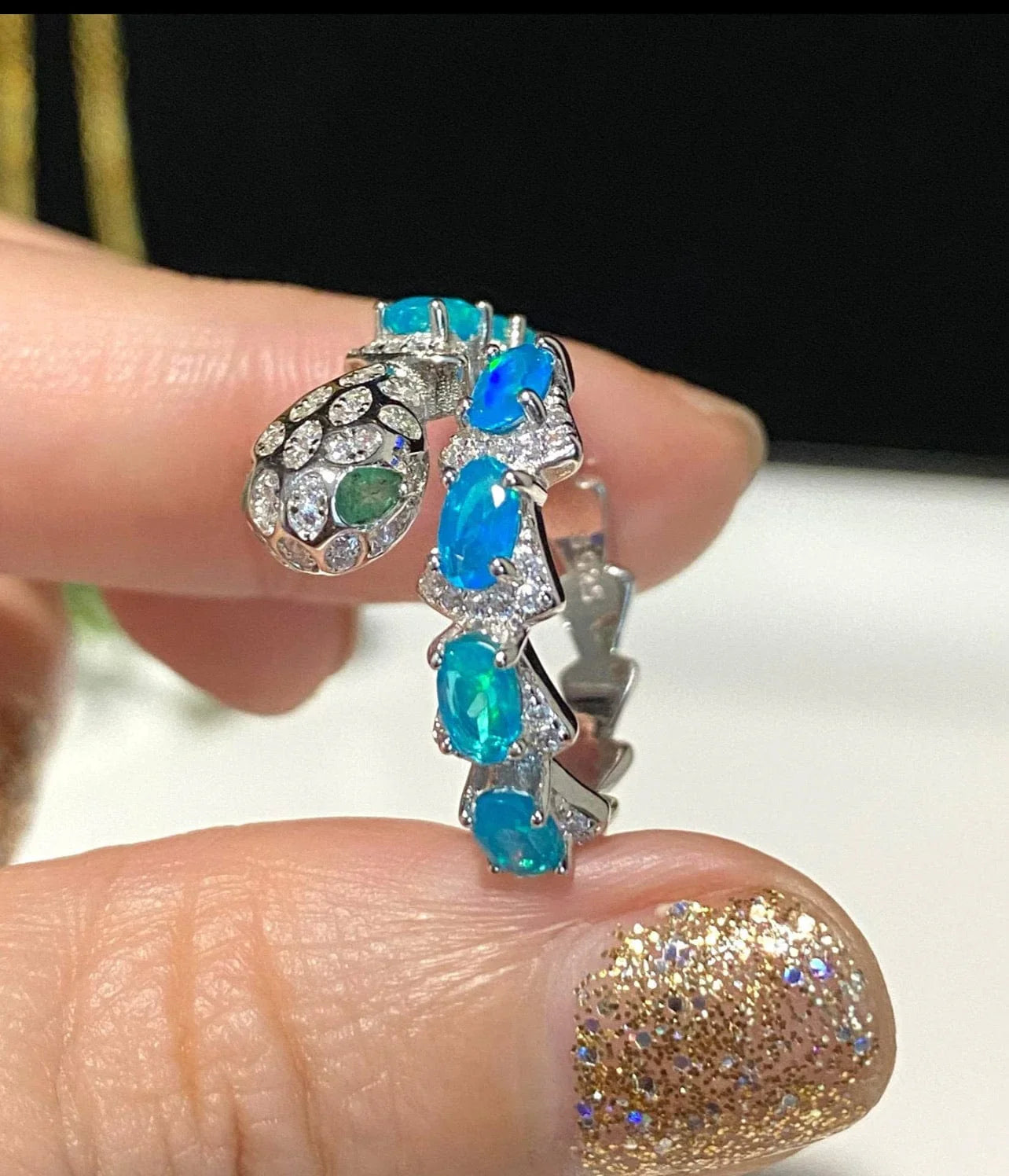 Portrait shot of a hand holding a captivating blue opal snake ring, emphasizing its unique artistry and stones.
