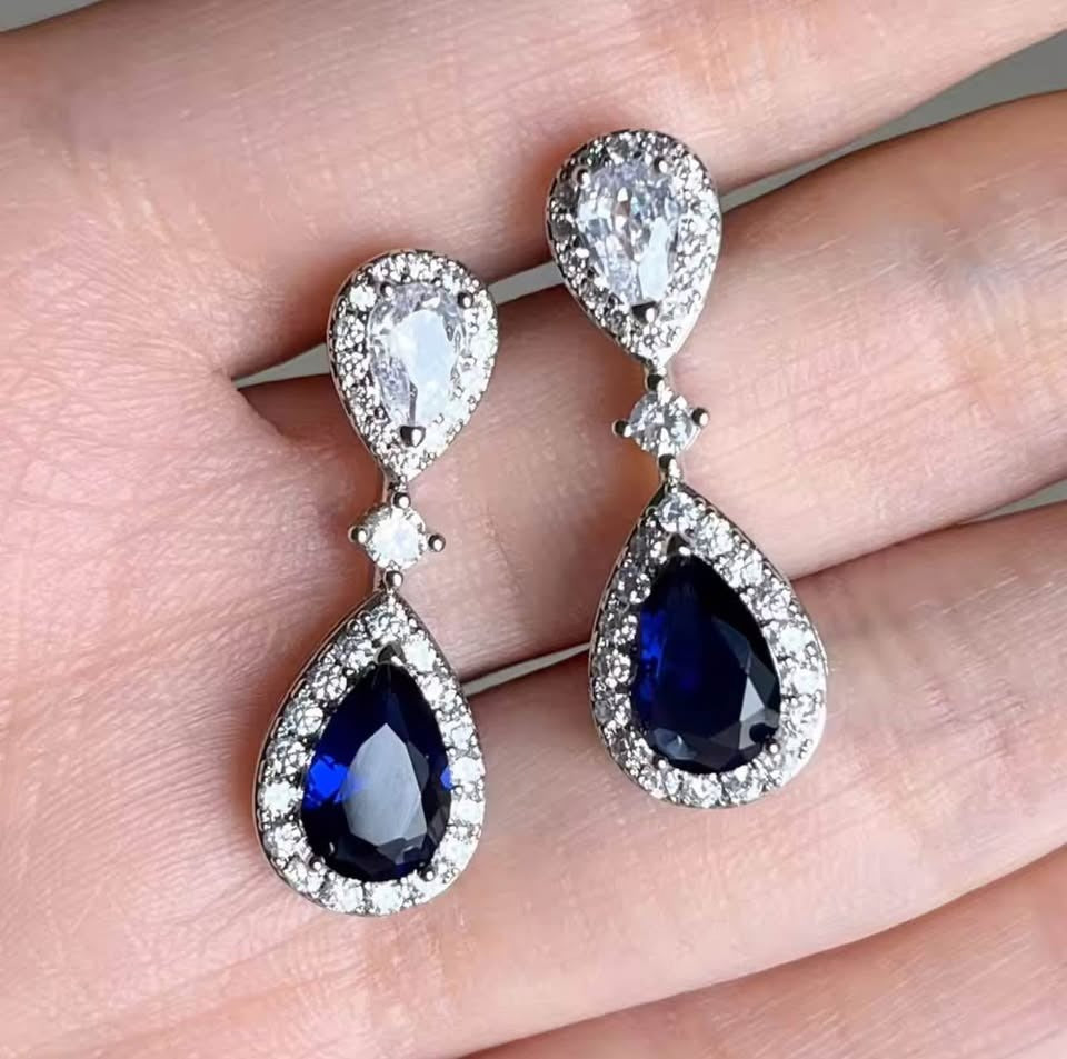 Elegant blue sapphire and diamond halo dangle earrings held in a hand, perfect for bridal wear.