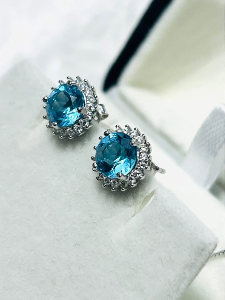  Side view of blue topaz halo earrings, highlighting the intricate rhodium-plated sterling silver work.