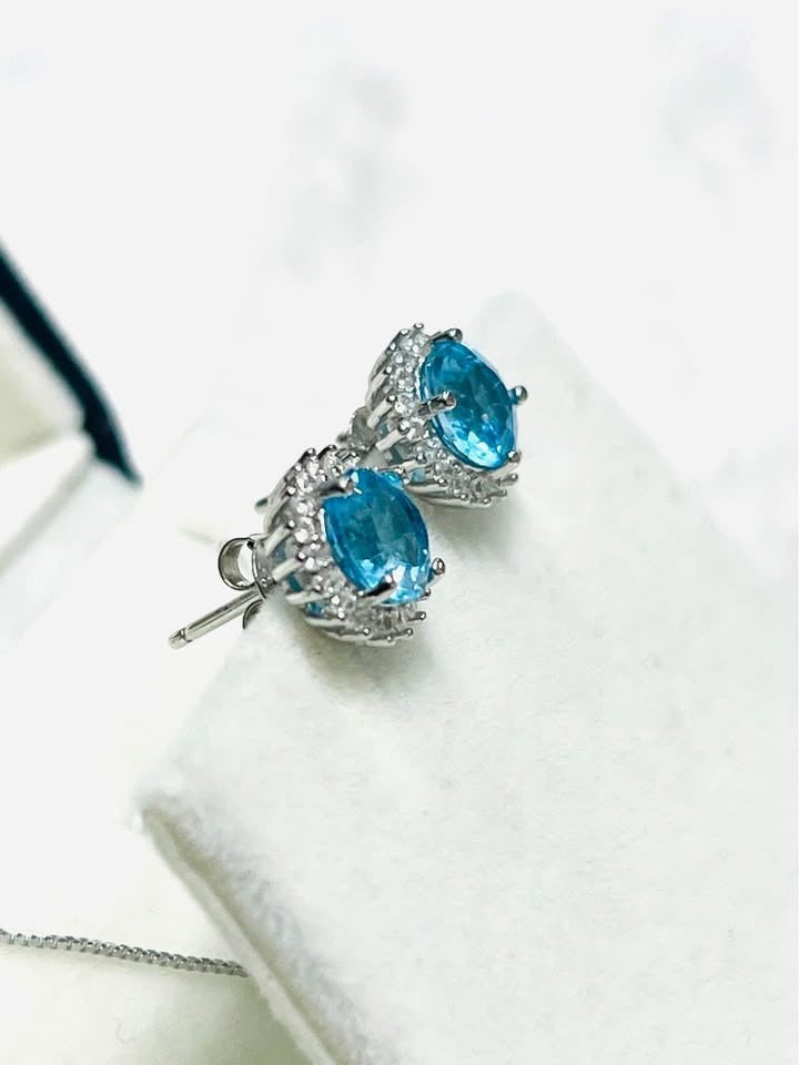 Oval blue topaz halo earrings, sterling silver with rhodium plating. Elegant stud design.