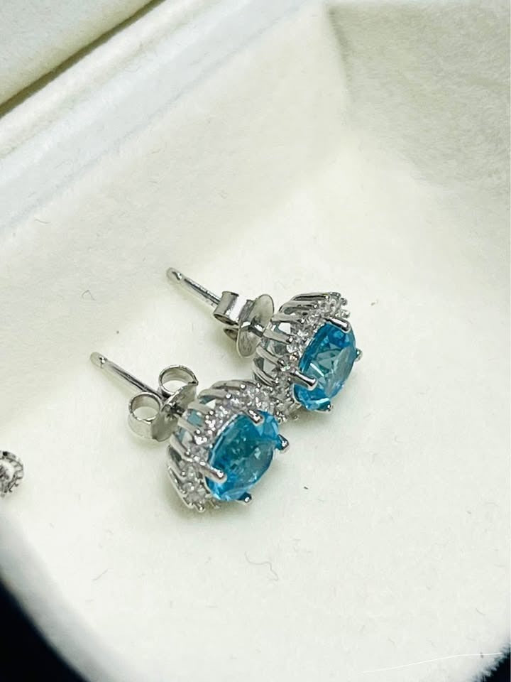 Close-up of elegant blue topaz stud earrings, showing secure backings and halo setting.