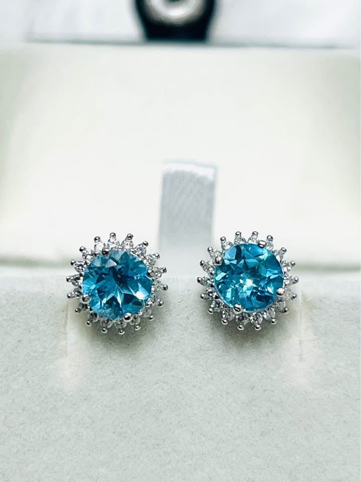 Detailed close-up of two blue topaz halo stud earrings, perfect for everyday elegance.