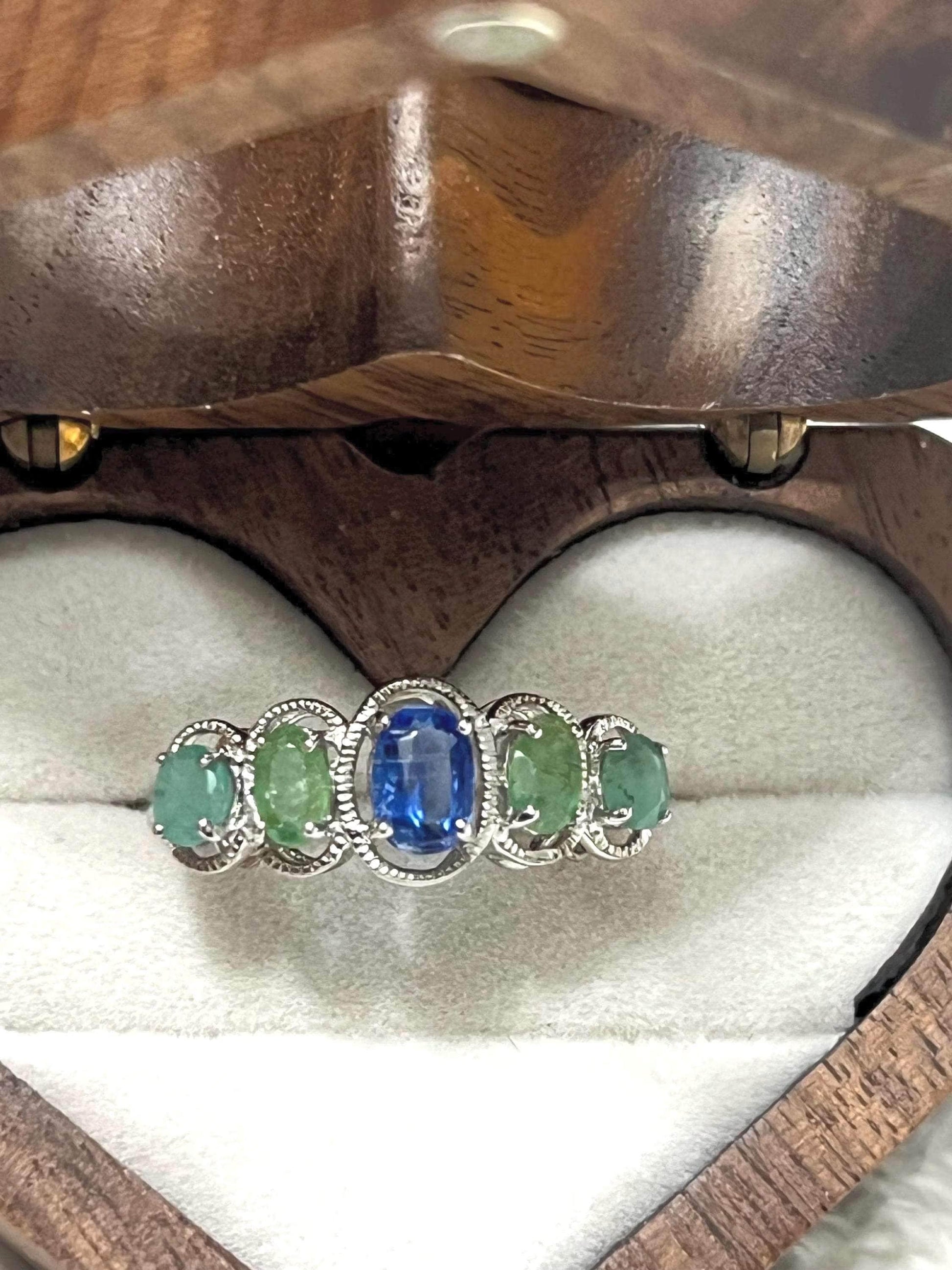 Bochic Kyanite and Colombian Emerald ring in a heart-shaped wooden box, showcasing vibrant gemstones.