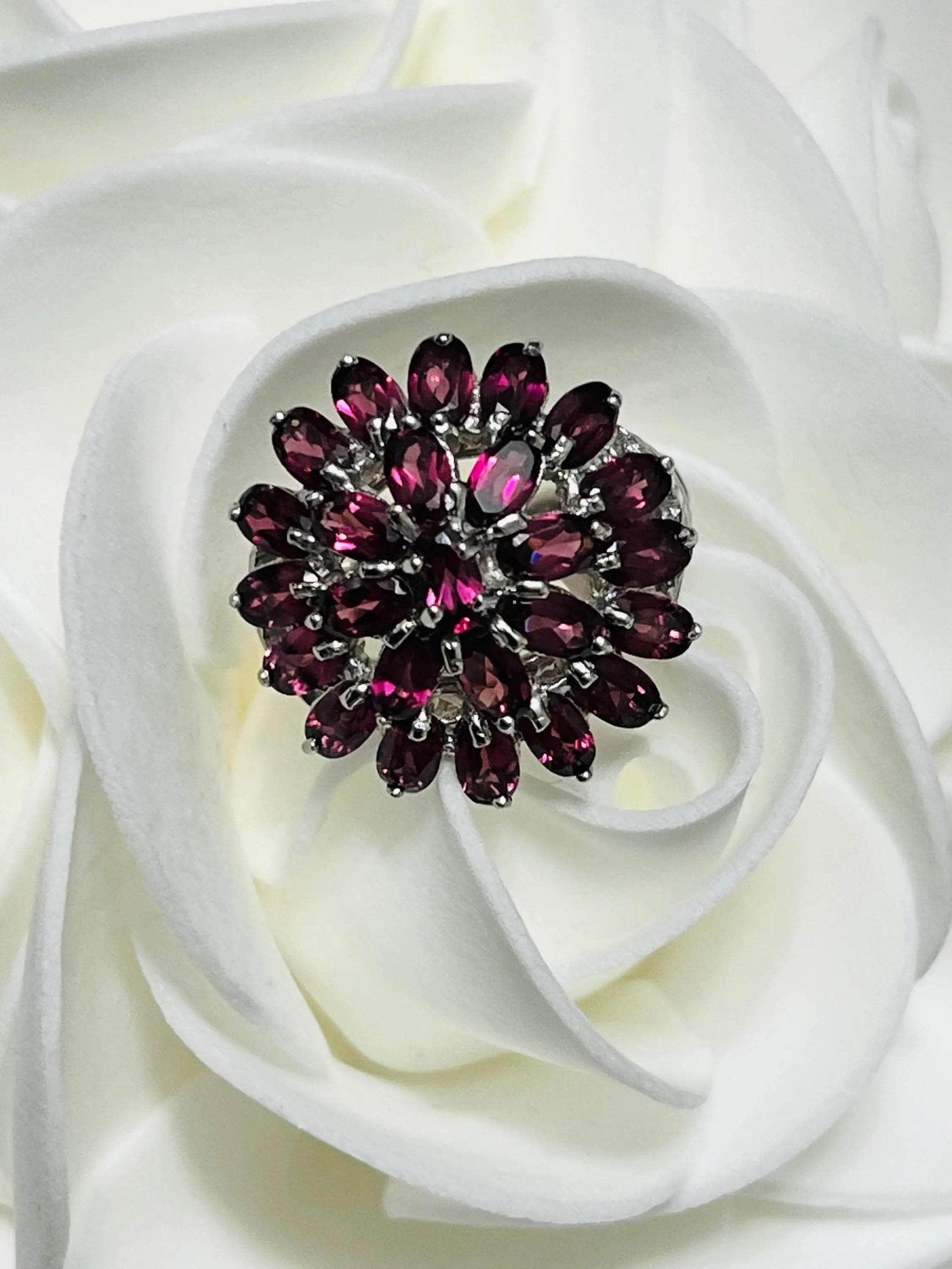 Close-up of Bochic vintage rhodolite garnet ring on a white rose, emphasizing gemstone clarity and cluster details