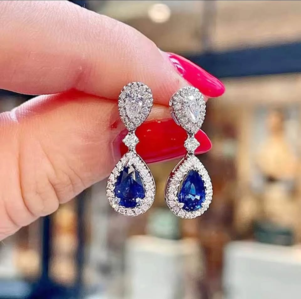 Close-up of stunning bridal blue sapphire teardrop earrings with sparkling diamond accents, held by hand.