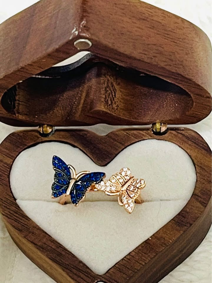 Stunning dual butterfly ring with blue and clear pavé stones, set in rose gold, inside a heart box.