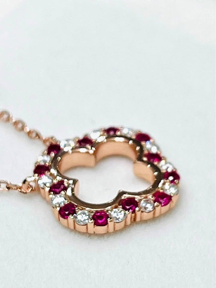 Macro shot of a rose gold clover pendant with vibrant ruby and brilliant moissanite gemstones.