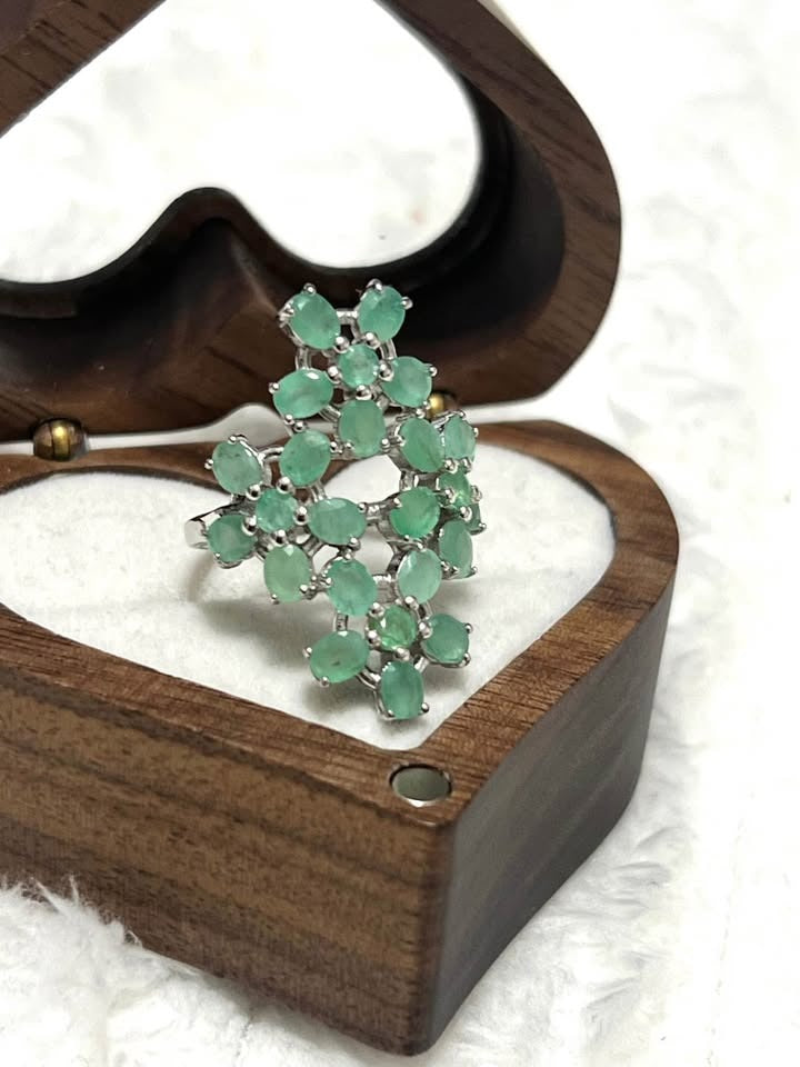 Intricate sterling silver ring adorned with natural Colombian emerald clusters, displayed in a heart-shaped wooden box.