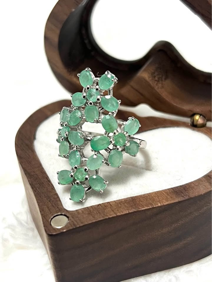 Elegant sterling silver ring with vibrant natural Colombian emeralds, beautifully presented in an open wooden jewelry box.