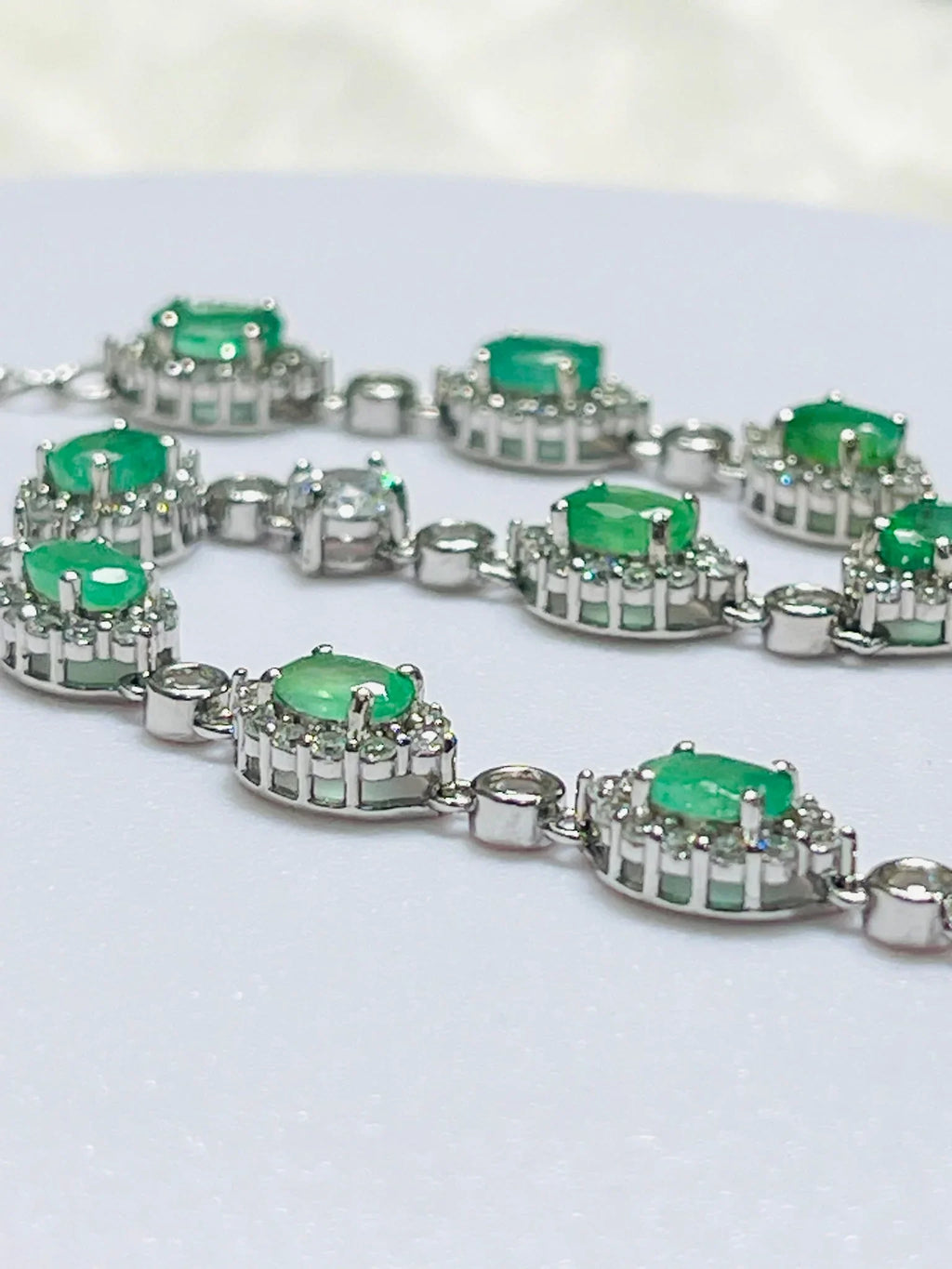 Close-up of handcrafted sterling silver bracelet with rhodium plating, showing oval Colombian emeralds in clear halo settings.